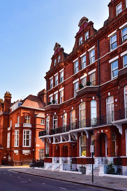 A street view of a red-brick residential building with multiple stories and white architectural accents, including arched windows and decorative cornices. The ground level features a stoop with steps 